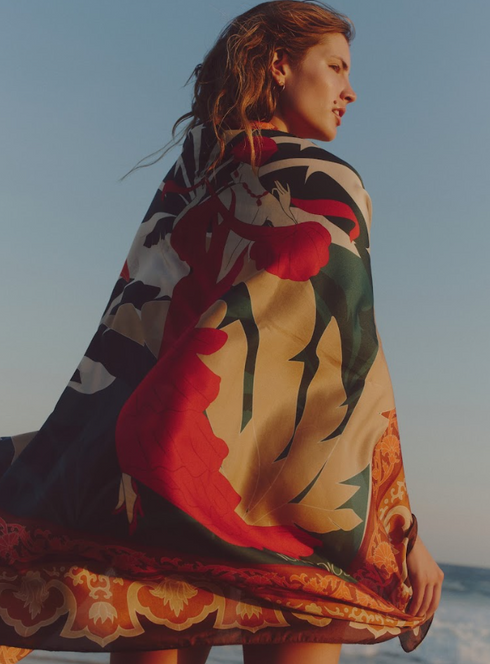 A woman wears a patterned cotton silk sarong in peach dancer with a large floral and figure design.