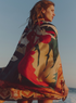 A woman wears a patterned cotton silk sarong in peach dancer with a large floral and figure design.