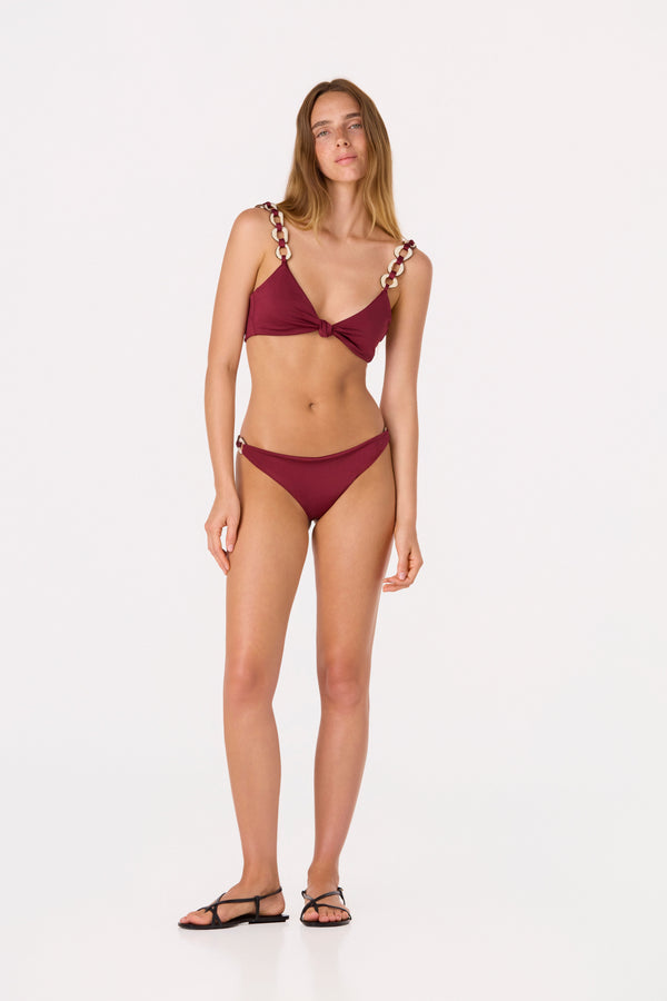 Woman wearing a low-rise purple bikini bottom with tagua side details and a matching top.