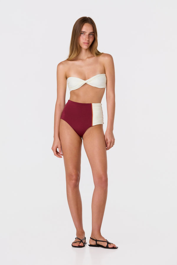Woman wearing a strapless ivory twist-front bikini top and high-waisted burgundy bottoms.