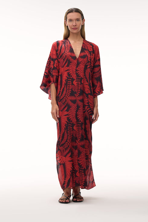 A woman wears a floor-length silk jacquard tunic in a red and black cherry rainforest print.