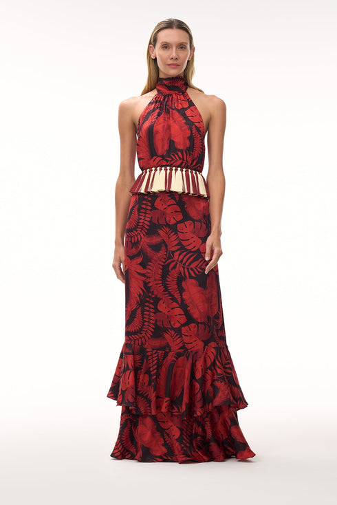 A woman wears a cherry red rainforest print silk jacquard maxi dress with a fringed waist detail.