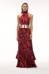A woman wears a cherry red rainforest print silk jacquard maxi dress with a fringed waist detail.