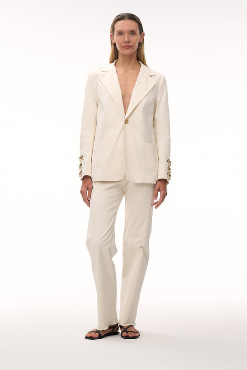 Woman wearing an ivory canvas blazer with hand-embroidered sleeve details and matching trousers.